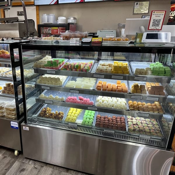 A brightly lit display case at Chaat House filled with rows of colorful Pakistani sweets and desserts.