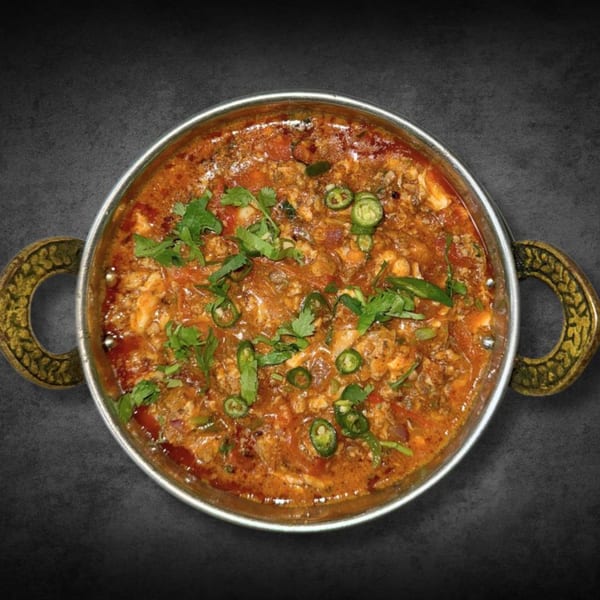 Chaat House's Pakistani chicken karahi, garnished with cilantro and green chilies, in a traditional metal bowl.