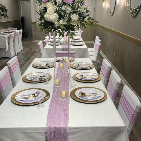 Elegantly set dining tables with white tablecloths, gold chargers, and purple accents for a special event.