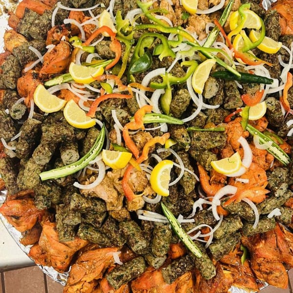 A large platter of Pakistani seekh kebabs and chicken tikka, garnished with onions, peppers, and lemons.