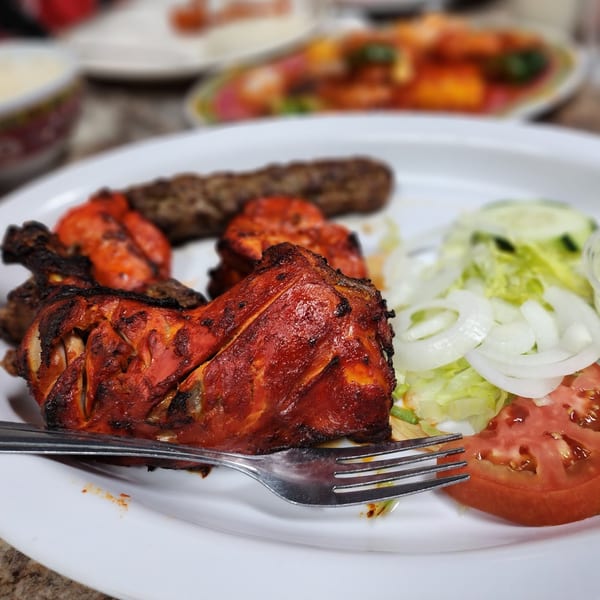 Chaat House's Pakistani grilled chicken, seekh kebab, and fresh salad on a white plate.