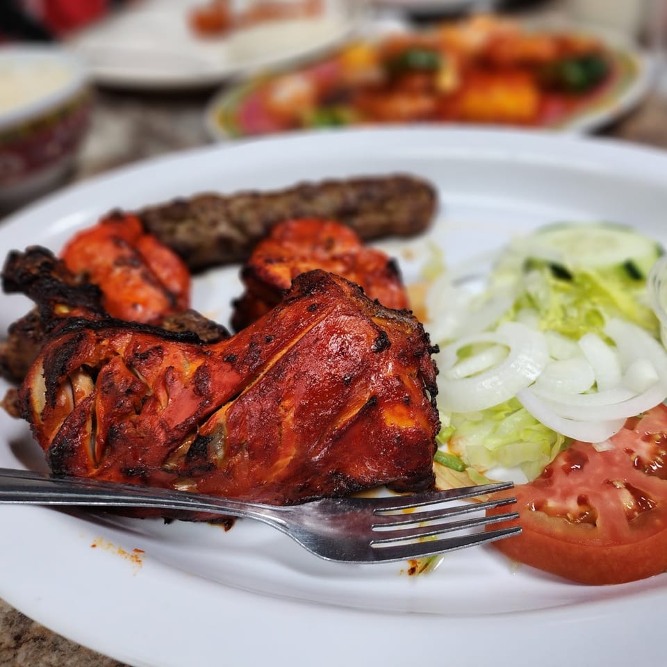 Chaat House's Pakistani grilled chicken, seekh kebab, and fresh salad on a white plate.