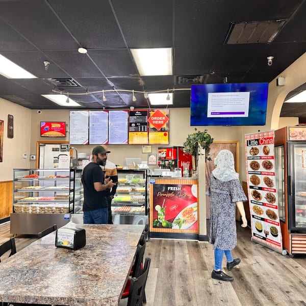 Customers ordering at the counter of Chaat House, with display cases of Pakistani sweets and menu boards.