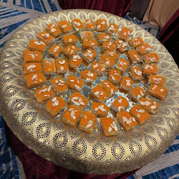 A golden ornate tray filled with individual servings of orange Pakistani halwa topped with sliced almonds.