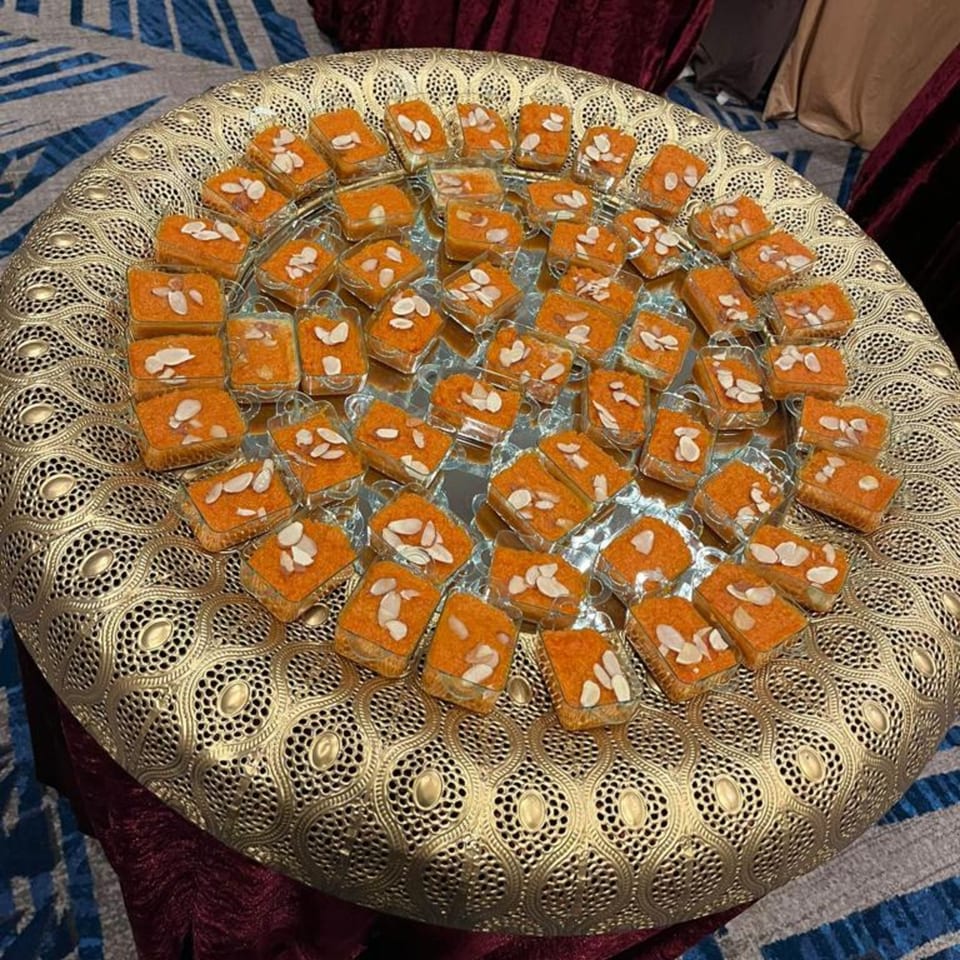 A golden ornate tray filled with individual servings of orange Pakistani halwa topped with sliced almonds.