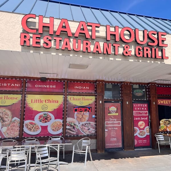 Exterior of Chaat House Restaurant & Grill with outdoor seating and window advertisements for Pakistani, Chinese, and Indian food.