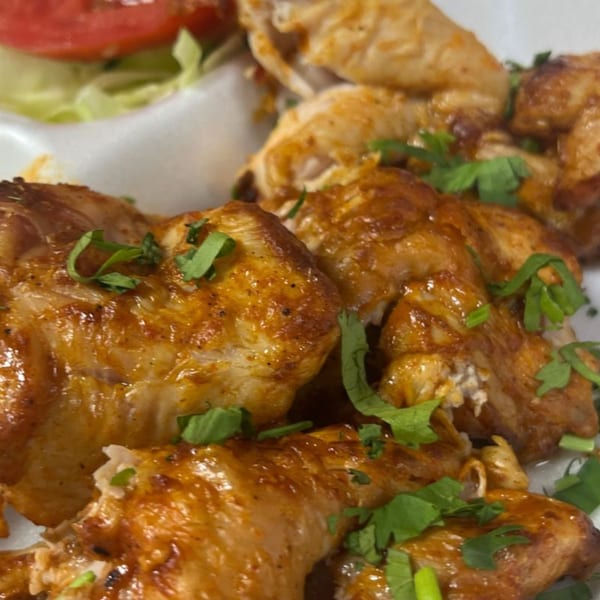 Close-up of golden-brown Pakistani grilled chicken pieces garnished with fresh cilantro and a side salad.