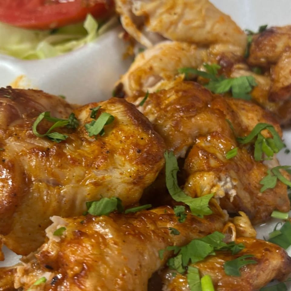 Close-up of golden-brown Pakistani grilled chicken pieces garnished with fresh cilantro and a side salad.