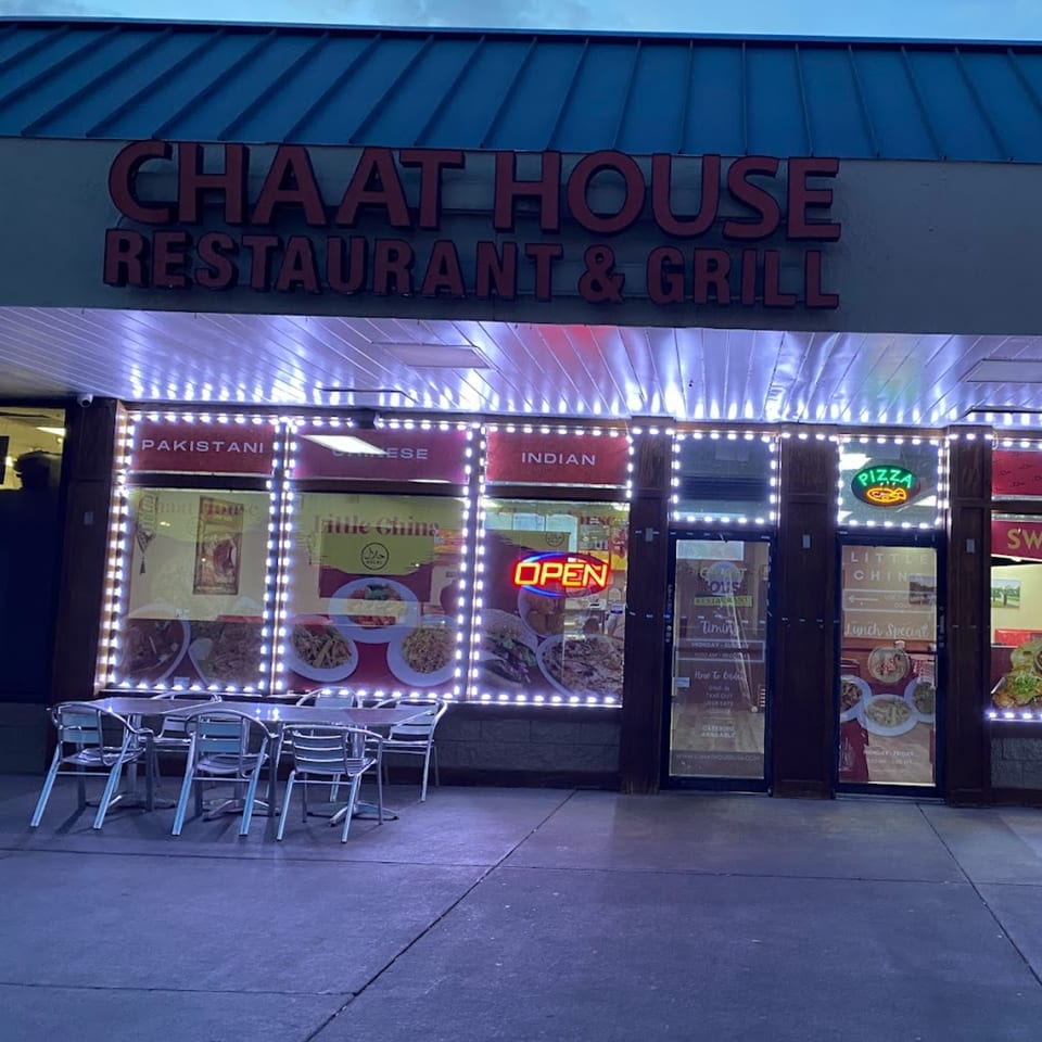 Chaat House Restaurant & Grill exterior at dusk, with bright lights, outdoor seating, and menu displays.