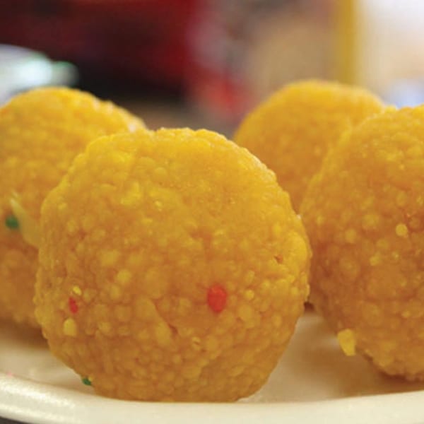 Close-up of several golden-yellow Pakistani Laddoo sweets with colorful sprinkles on a white plate.