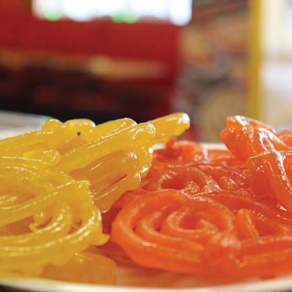 Close-up of vibrant orange and yellow jalebi, a traditional Pakistani sweet, on a white plate.