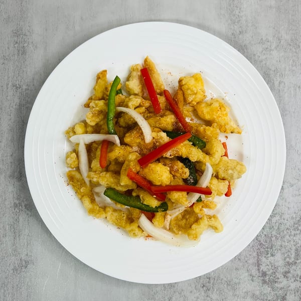 Crispy fried chicken pieces with red and green bell peppers and white onions on a white plate.