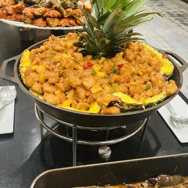 Pineapple chicken curry served in a pineapple shell, with other Pakistani dishes in the background.